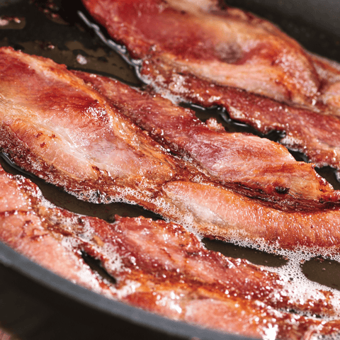 bacon slices being fried in a pan in bacon grease
