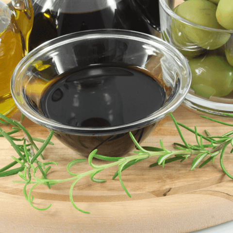 balsamic vinegar in glass dish surrounded by olives and oik