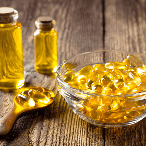 fish oil tablets in glass dish bowl next to wooden spoon 