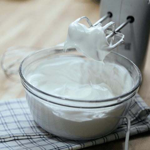 mixer dipped into freshly whipped cream in glass bowl