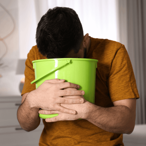 man in orange shirt gesturing to vomit into green bucket