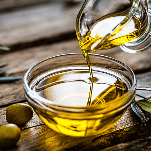 olive oil poured into glass dish next to olives
