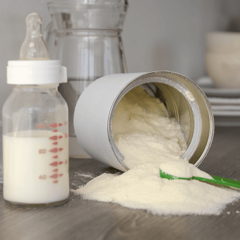 open baby formula tin next to baby bottle with milk