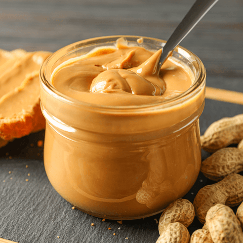 peanut butter in glass jar next to peanuts