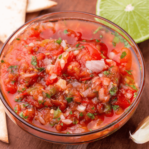 salsa in glass dish next to tortillas and limes